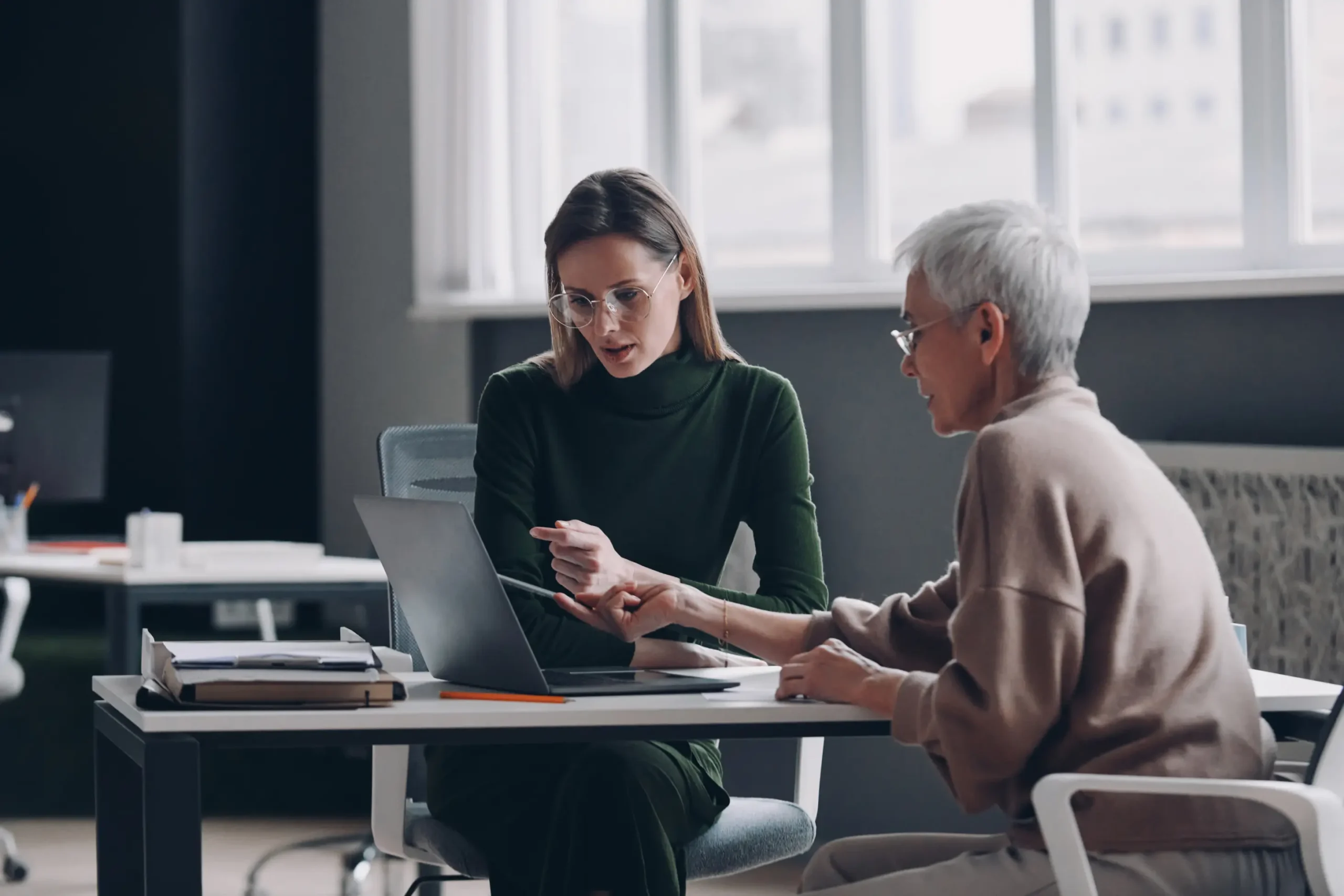 Two women collaborating over a laptop at desk.