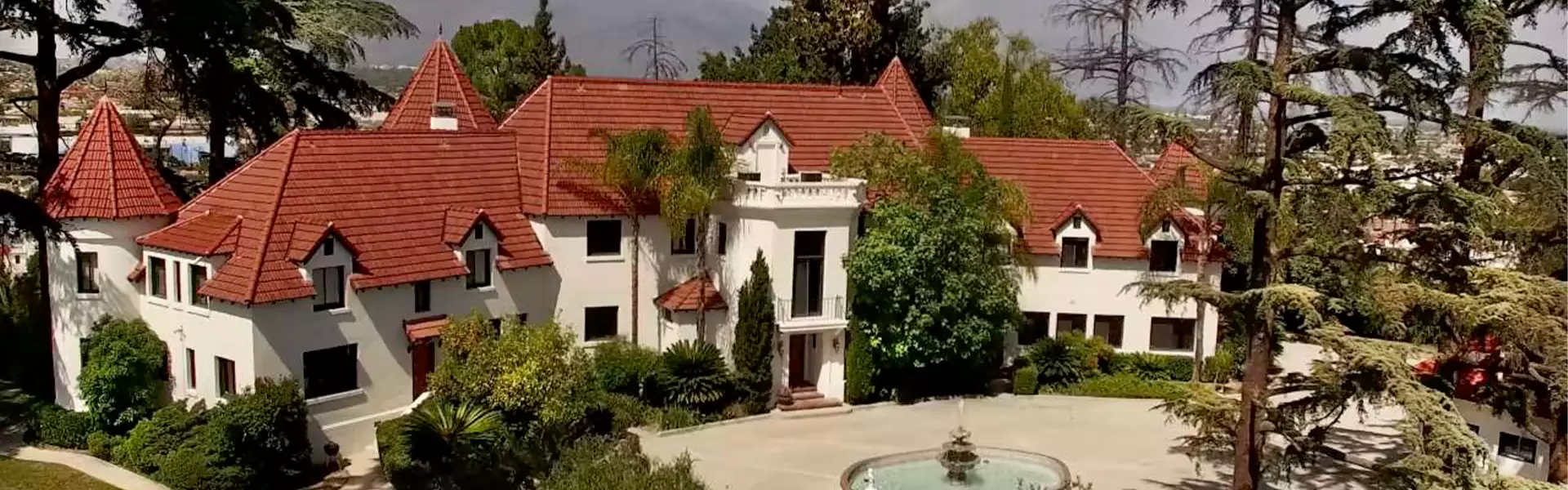 Elegant mansion with red tile roof and greenery.