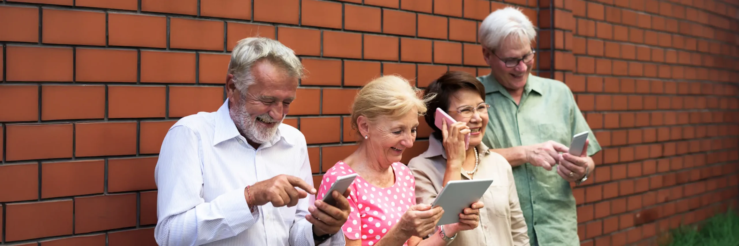 Seniors smiling while using smartphones and tablets outdoors.