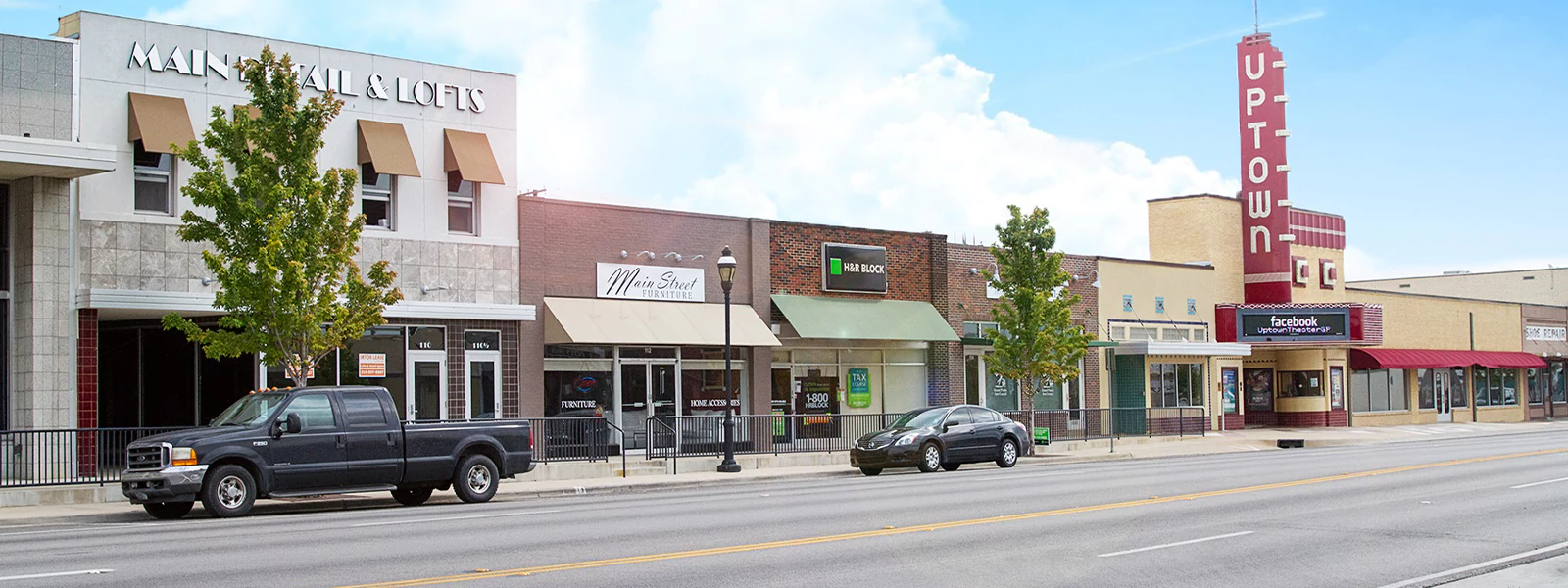 Main Street shops with trees and parked cars.