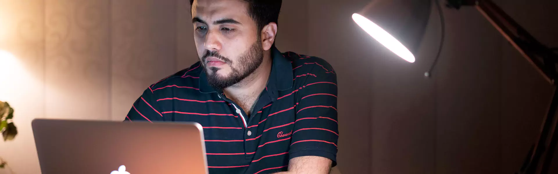 Man working on laptop under desk lamp.