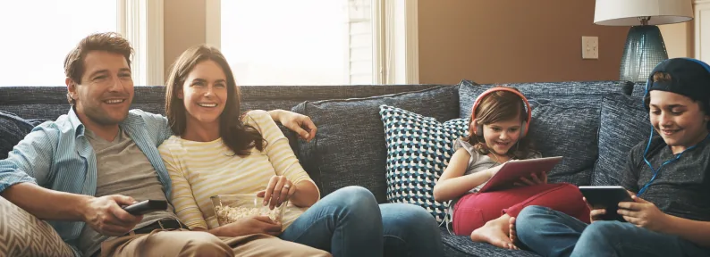 Family relaxing together on a couch, enjoying devices.