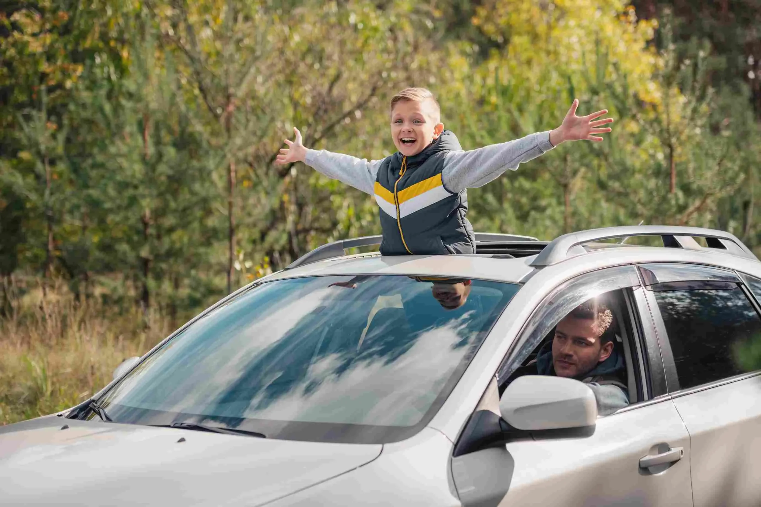 Boy joyfully leaning out of car sunroof.