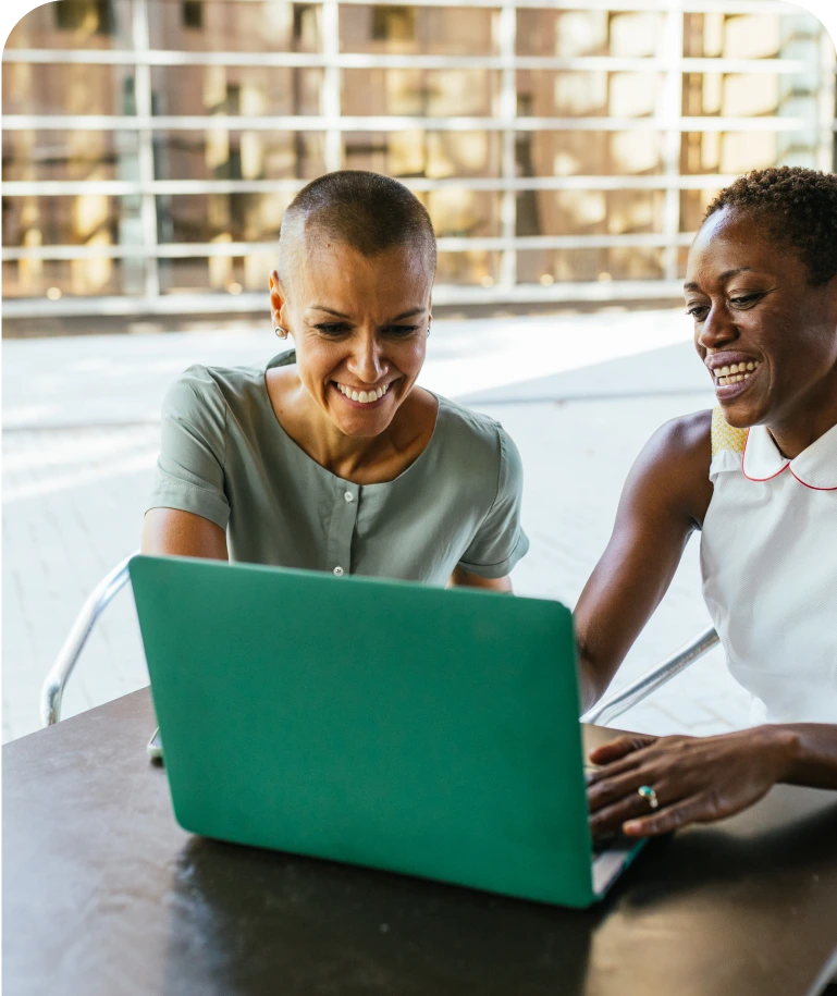 Two women collaborating on a green laptop