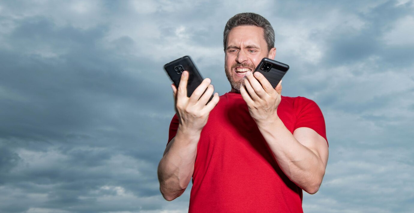 Man comparing two smartphones under cloudy sky.