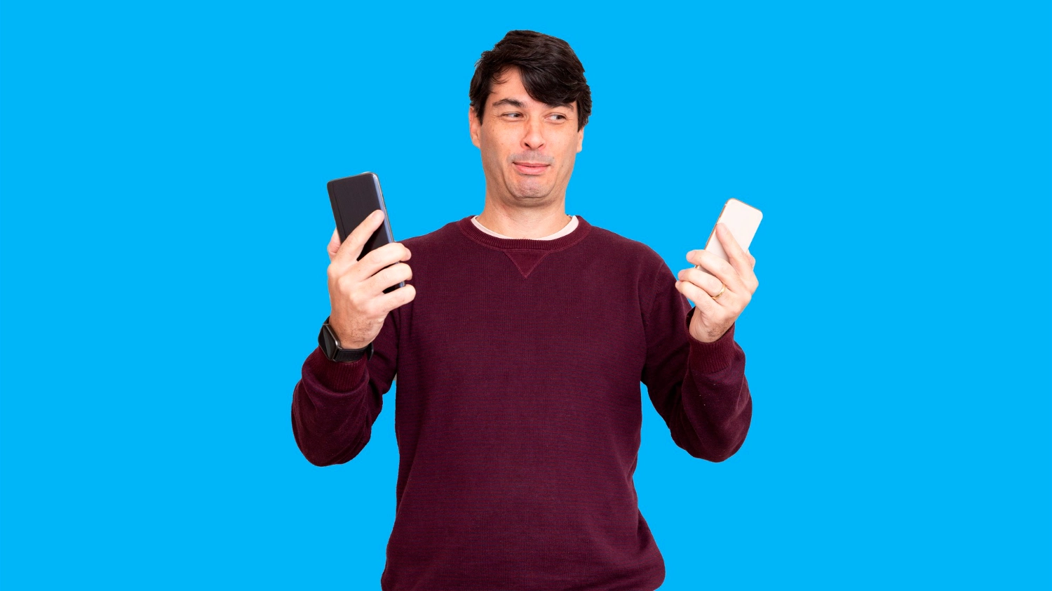 Man comparing two smartphones against blue background