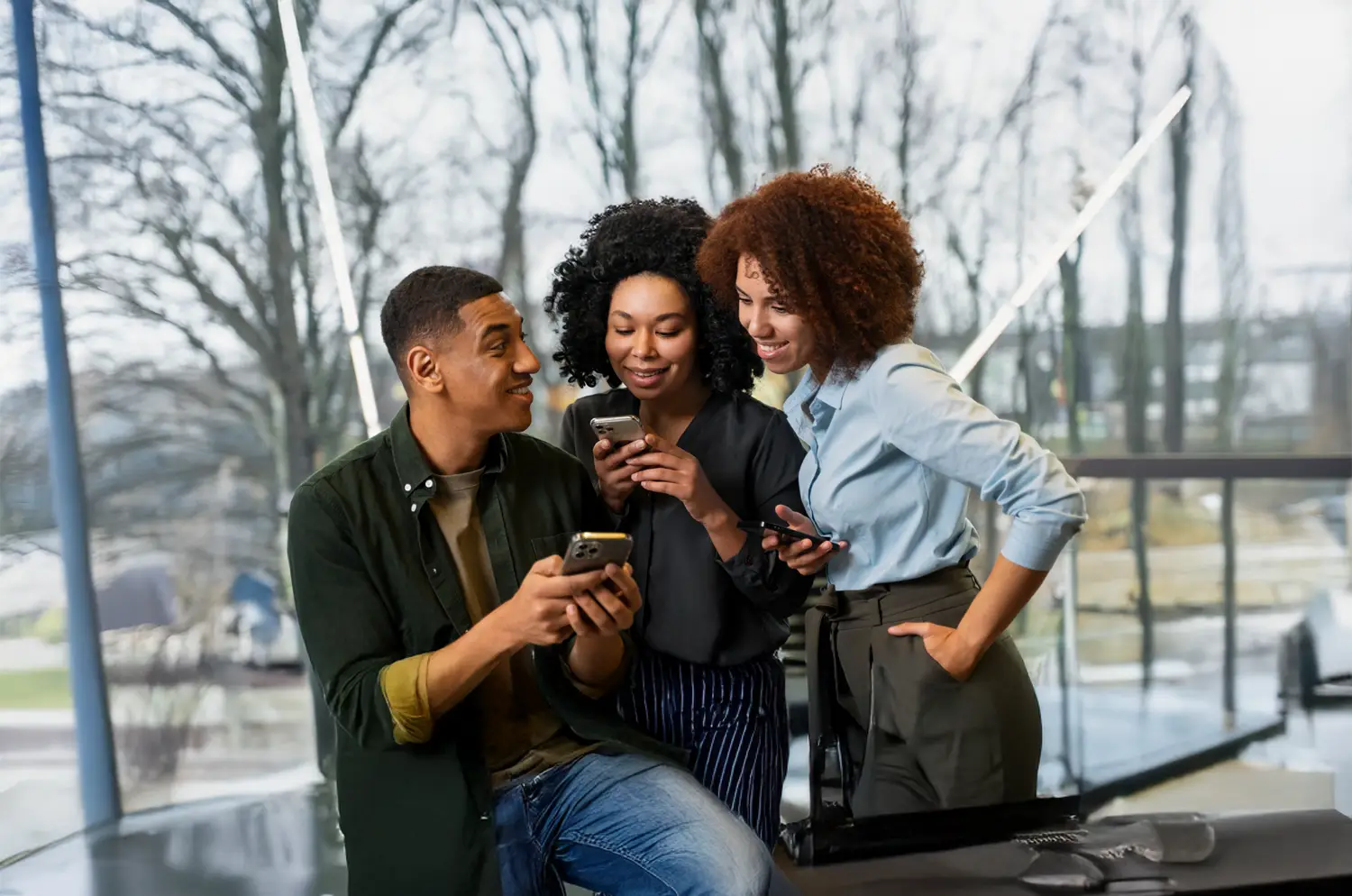Three friends laughing while using their smartphones.