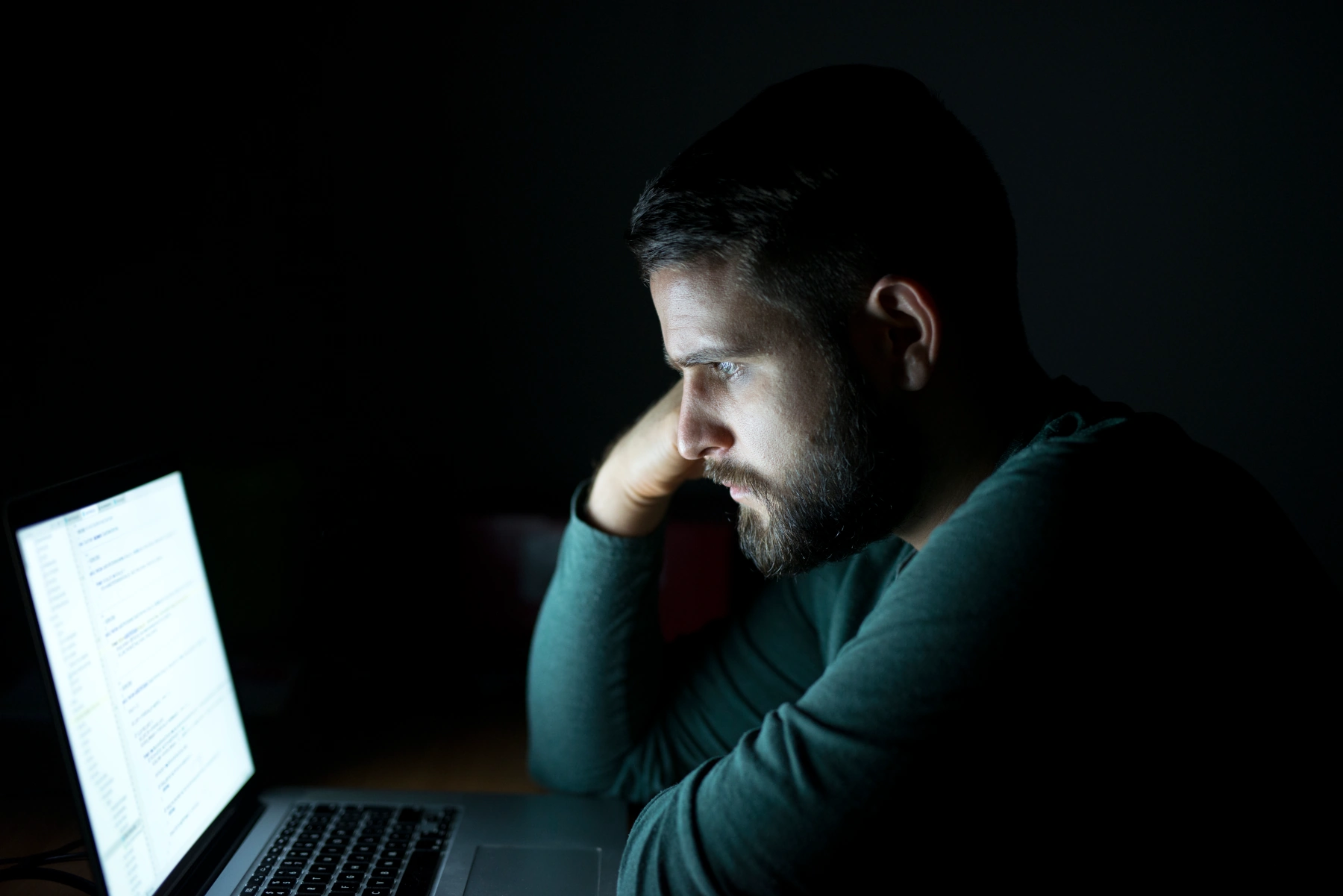 Man focused on laptop screen in dark room