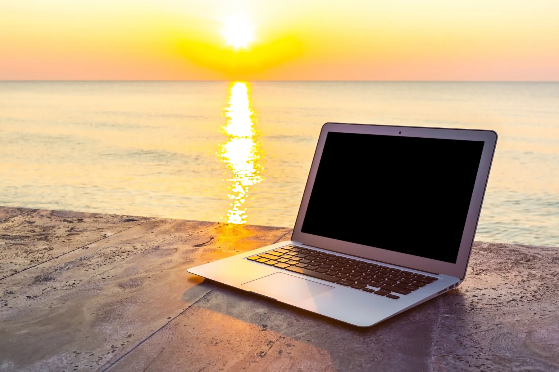Laptop on table by sunset over ocean.